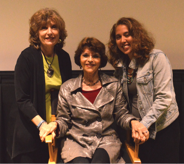 Dr. Harriet Fields with Dr. Linda Rhodes and Gina Izzo Dr. Harriet Fields sitting in directors chair with Dr. Linda Rhodes and Gina Izzo standing on either side.
