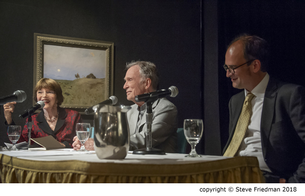 Candid photo of Harriet talking with panelists sitting at a table with microphones.