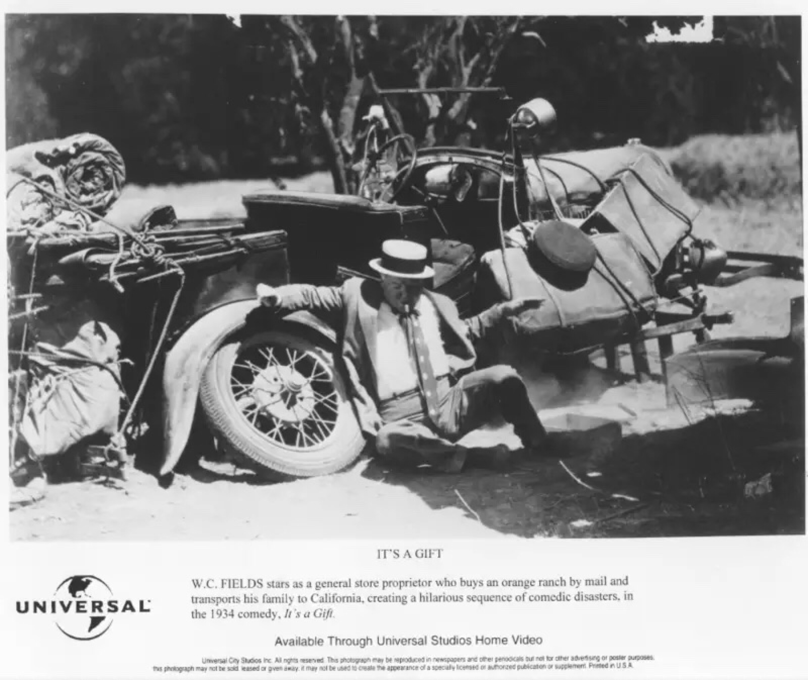 Still from It's a Gift of W.C. Fields sitting on the ground with his back to a broke down car.